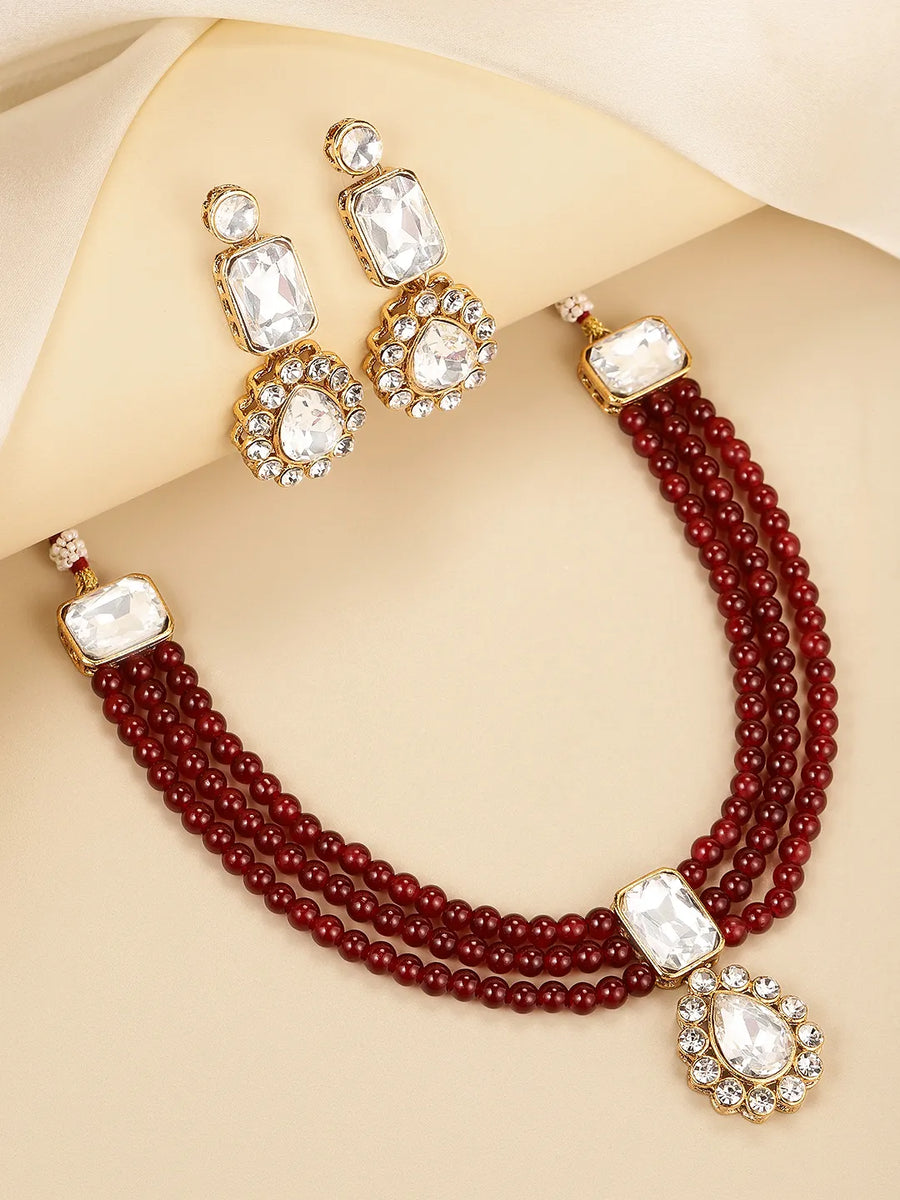 Graceful Layers with Kundan Set. Gold-plated red beaded necklace set with large white stones and matching drop earrings.