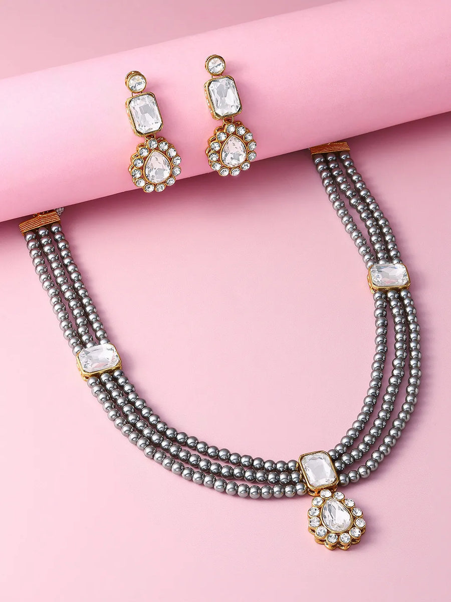 Gracefully Layered Kundan Necklace Set. Gold and grey pearl necklace set with matching drop earrings featuring rectangular stones and floral motifs.