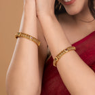 Woman wearing gold bracelets with rani pink accent on a beige background rom Peora