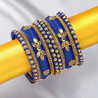 A set of blue and gold colored alloy bangles with kundan embellishments displayed on a cylindrical object.