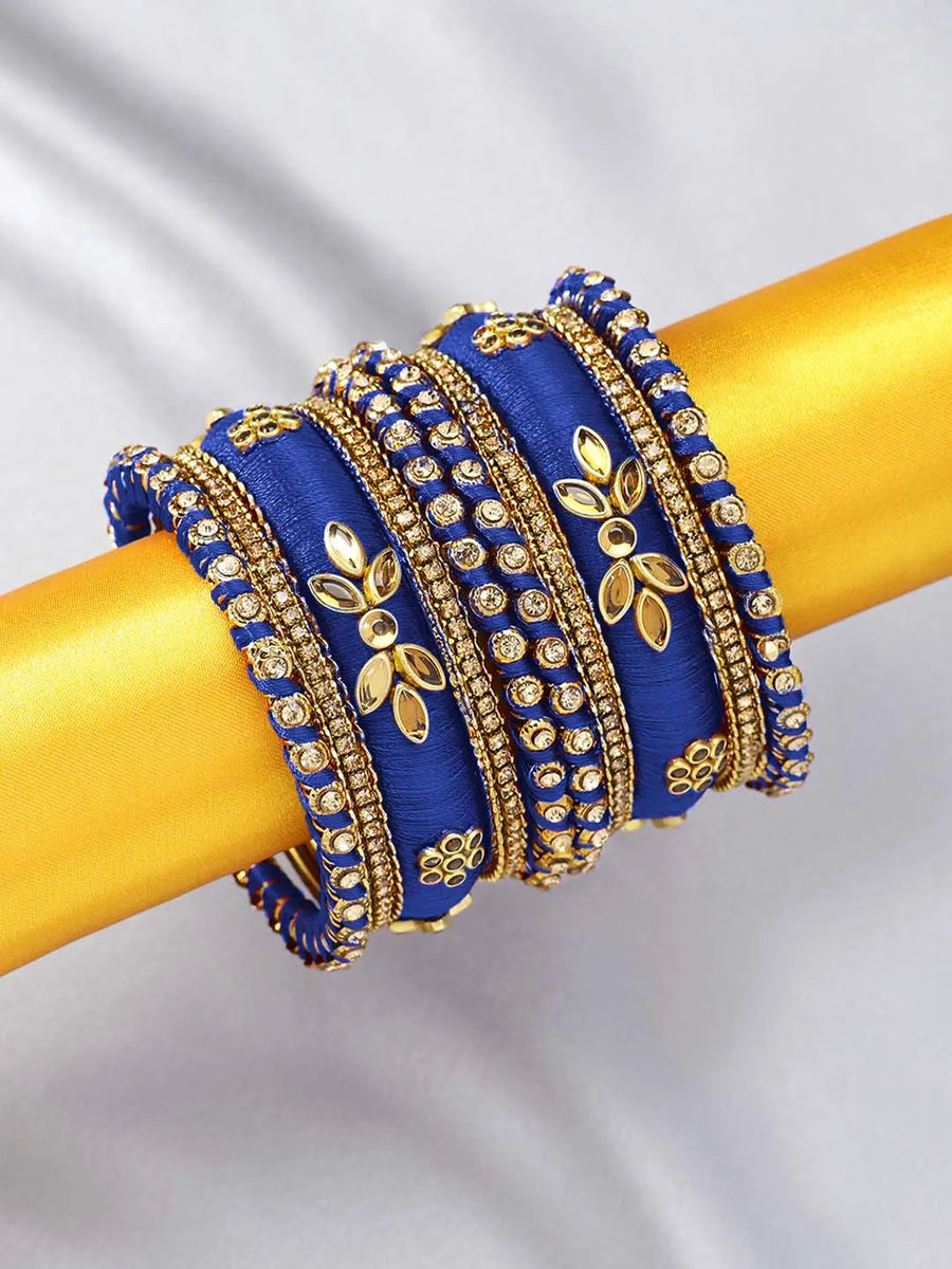 A set of blue and gold colored alloy bangles with kundan embellishments displayed on a cylindrical object.