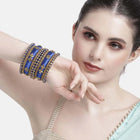A set of blue and gold colored alloy bangles with kundan embellishments displayed on a cylindrical object.