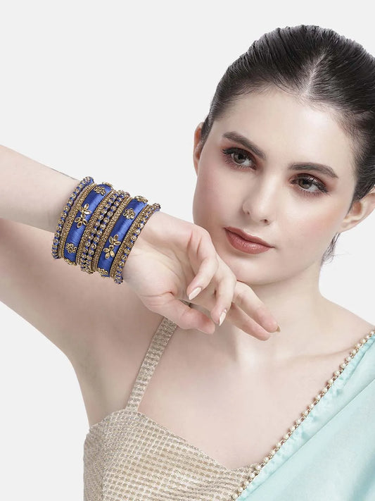 A set of blue and gold colored alloy bangles with kundan embellishments displayed on a cylindrical object.