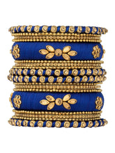 A set of blue and gold colored alloy bangles with kundan embellishments displayed on a cylindrical object.