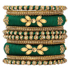 A set of Green and gold colored alloy bangles with kundan embellishments displayed on a cylindrical object.