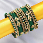 A set of Green and gold colored alloy bangles with kundan embellishments displayed on a cylindrical object.