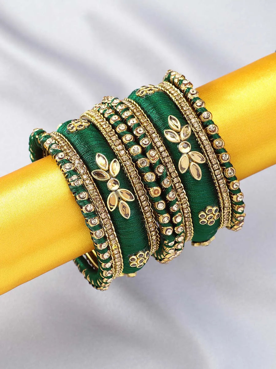 A set of Green and gold colored alloy bangles with kundan embellishments displayed on a cylindrical object.