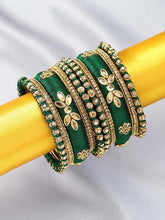 A set of Green and gold colored alloy bangles with kundan embellishments displayed on a cylindrical object.