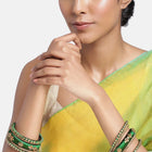 A set of Green and gold colored alloy bangles with kundan embellishments displayed on a cylindrical object.