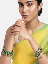 A set of Green and gold colored alloy bangles with kundan embellishments displayed on a cylindrical object.