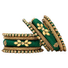 A set of Green and gold colored alloy bangles with kundan embellishments displayed on a cylindrical object.