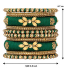 A set of Green and gold colored alloy bangles with kundan embellishments displayed on a cylindrical object.