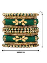 A set of Green and gold colored alloy bangles with kundan embellishments displayed on a cylindrical object.