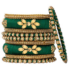 A set of Green and gold colored alloy bangles with kundan embellishments displayed on a cylindrical object.