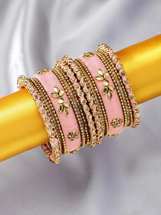 A set of Peach and gold colored alloy bangles with kundan embellishments displayed on a cylindrical object.