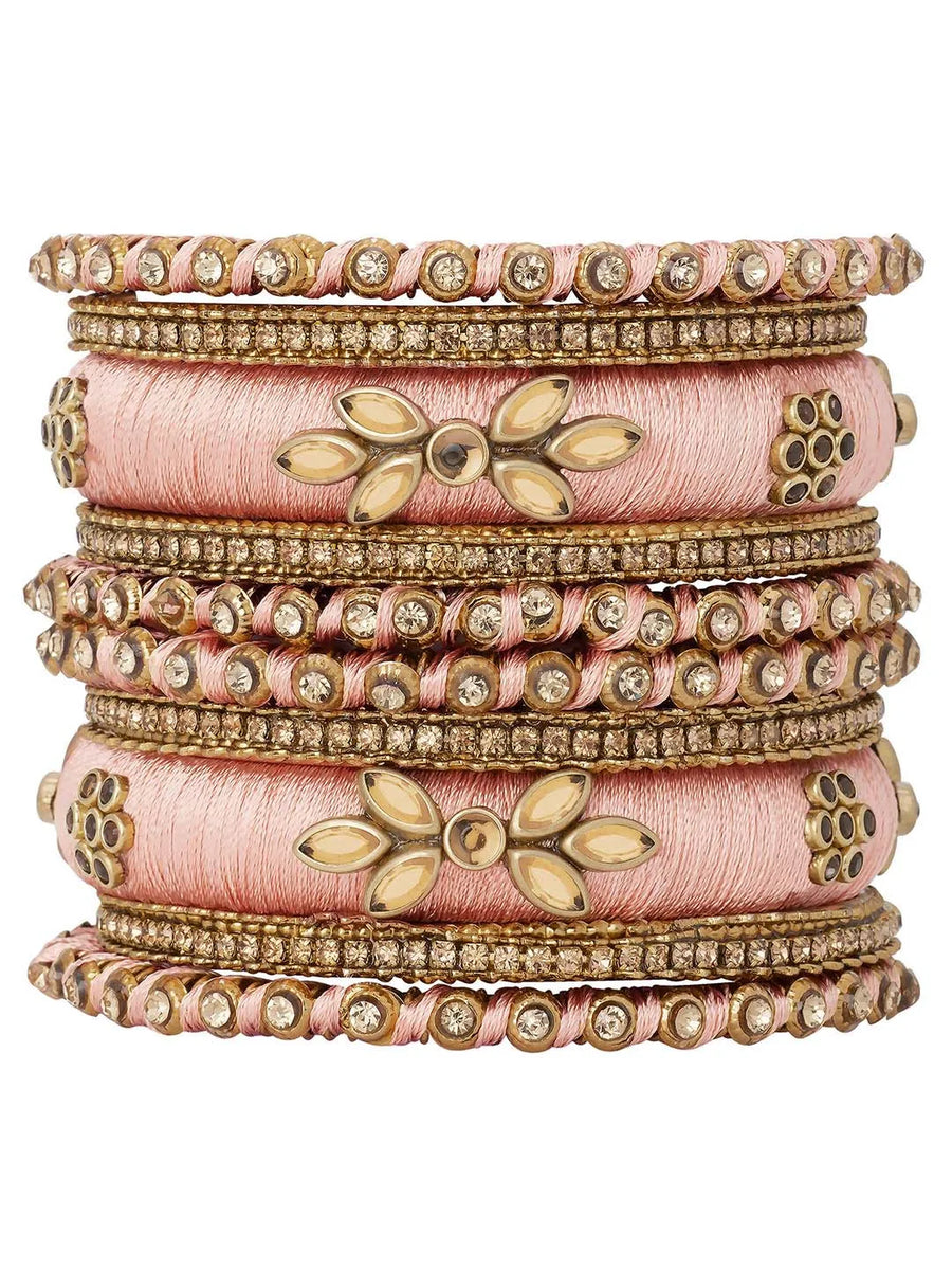 A set of Peach and gold colored alloy bangles with kundan embellishments displayed on a cylindrical object.