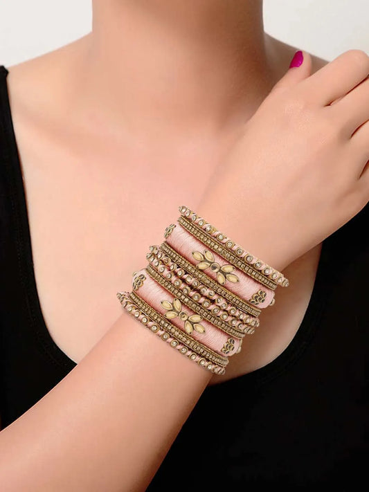 A set of Peach and gold colored alloy bangles with kundan embellishments displayed on a cylindrical object.