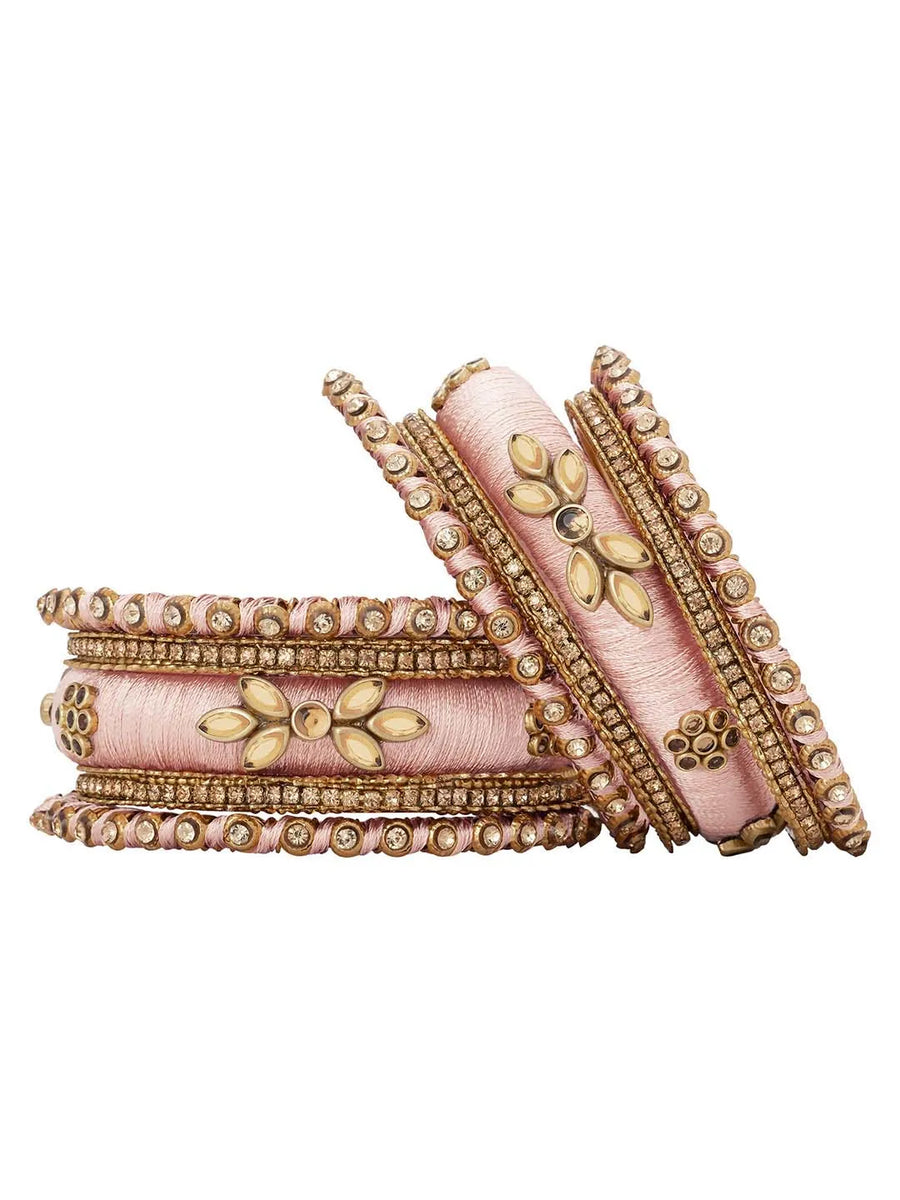 A set of Peach and gold colored alloy bangles with kundan embellishments displayed on a cylindrical object.