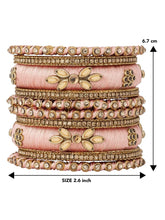 A set of Peach and gold colored alloy bangles with kundan embellishments displayed on a cylindrical object.