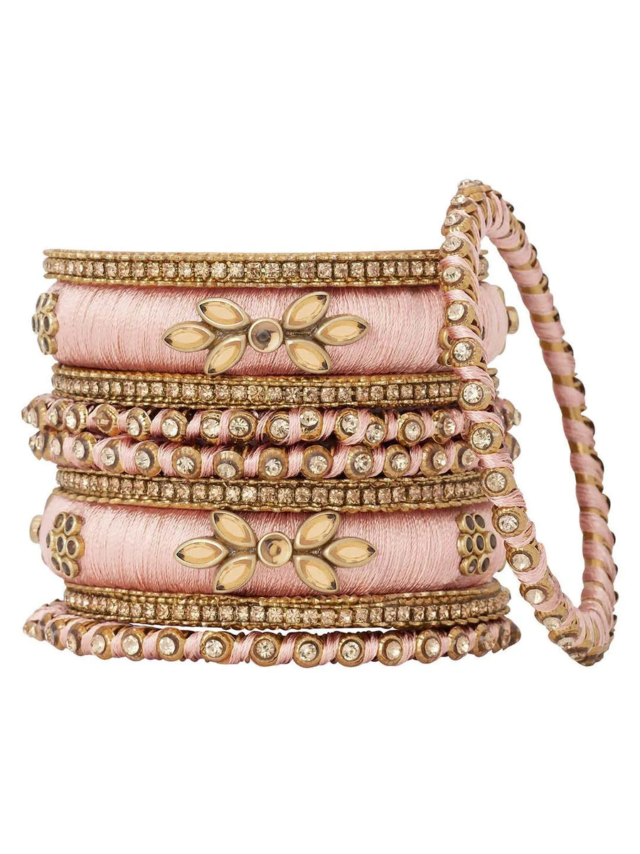 A set of Peach and gold colored alloy bangles with kundan embellishments displayed on a cylindrical object.