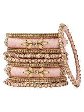 A set of Peach and gold colored alloy bangles with kundan embellishments displayed on a cylindrical object.