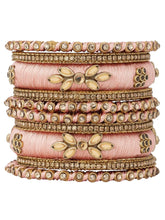 A set of Peach and gold colored alloy bangles with kundan embellishments displayed on a cylindrical object.