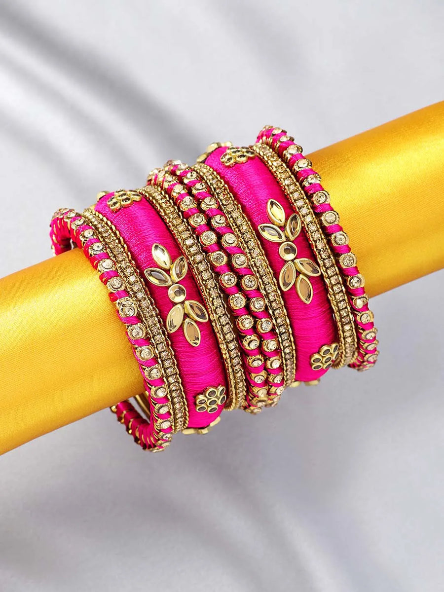 A set of Pink and gold colored alloy bangles with kundan embellishments displayed on a cylindrical object.