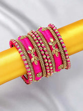 A set of Pink and gold colored alloy bangles with kundan embellishments displayed on a cylindrical object.