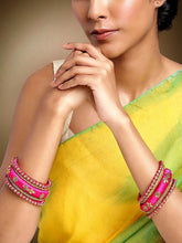 A set of Pink and gold colored alloy bangles with kundan embellishments displayed on a cylindrical object.