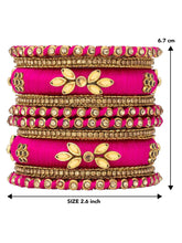 A set of Pink and gold colored alloy bangles with kundan embellishments displayed on a cylindrical object.
