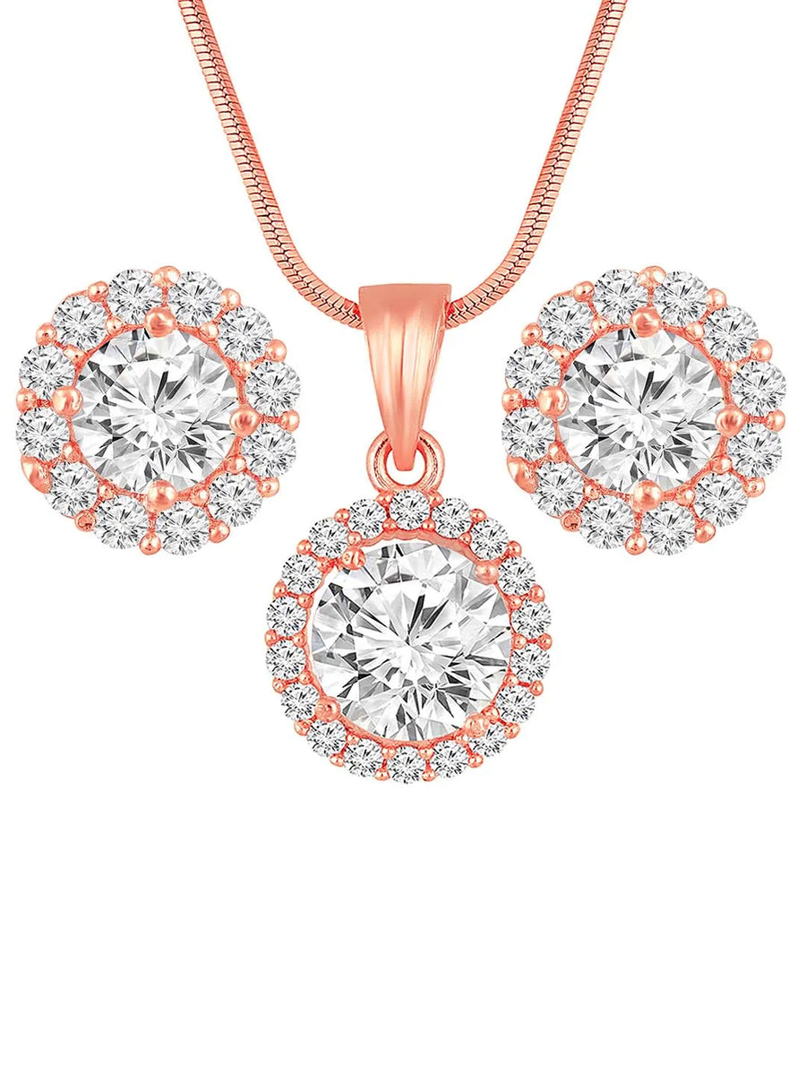 A rose gold-colored pendant necklace with a round cubic zirconia solitaire pendant accompanied by a pair of matching earrings, displayed on a pink cushion.