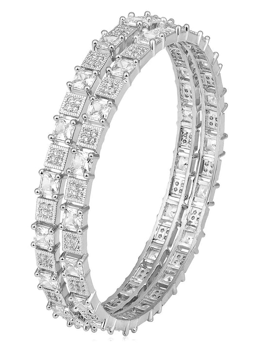 A set of two silver-colored bangles adorned with cubic zirconia stones, displayed against a dark background with floral patterns.
