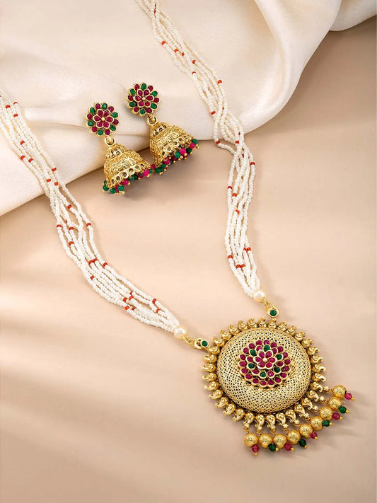 A traditional Indian necklace set with gold-colored metalwork and synthetic stones, accompanied by matching earrings, displayed on a white fabric surface.