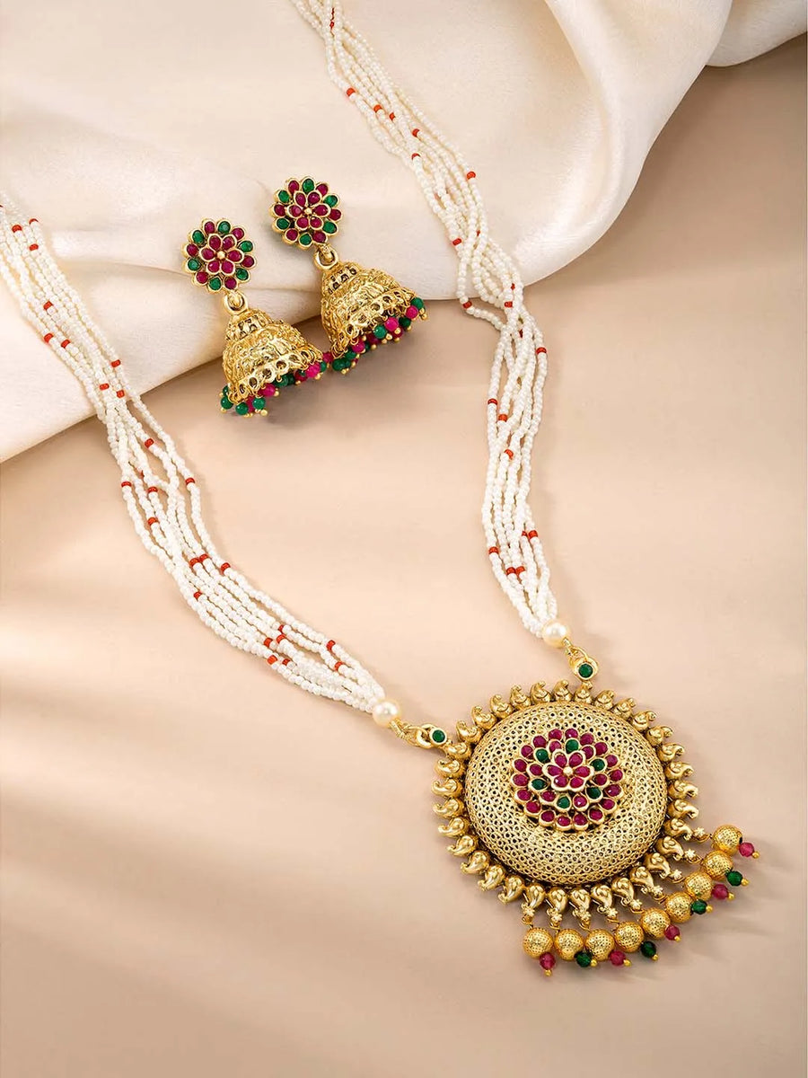 A traditional Indian necklace set with gold-colored metalwork and synthetic stones, accompanied by matching earrings, displayed on a white fabric surface.