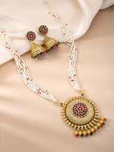 A traditional Indian necklace set with gold-colored metalwork and synthetic stones, accompanied by matching earrings, displayed on a white fabric surface.