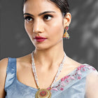 A traditional Indian necklace set with gold-colored metalwork and synthetic stones, accompanied by matching earrings, displayed on a white fabric surface.