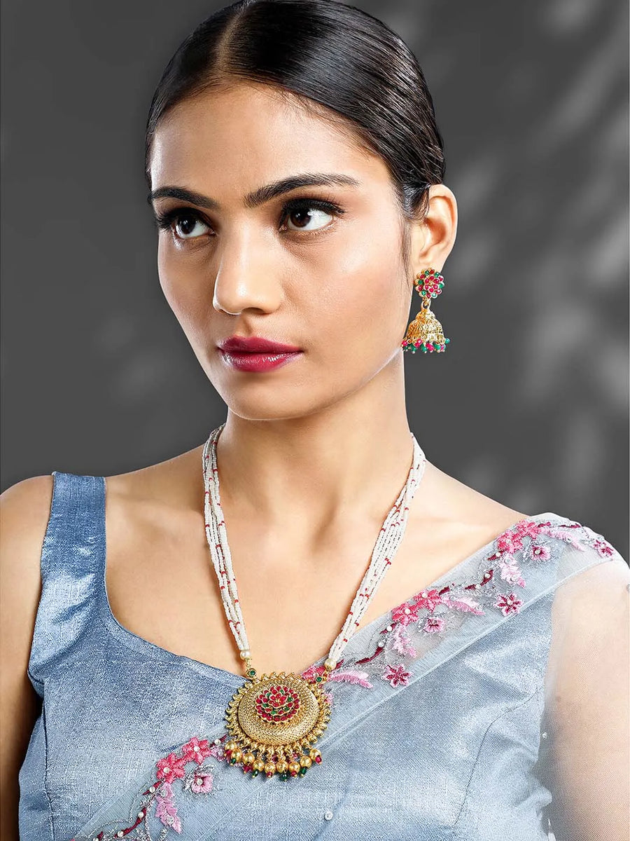 A traditional Indian necklace set with gold-colored metalwork and synthetic stones, accompanied by matching earrings, displayed on a white fabric surface.