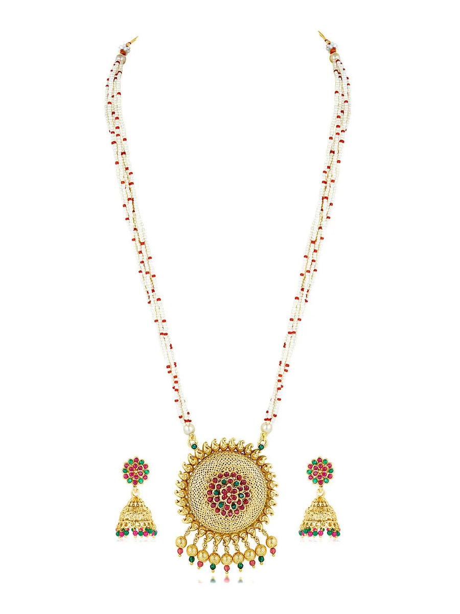 A traditional Indian necklace set with gold-colored metalwork and synthetic stones, accompanied by matching earrings, displayed on a white fabric surface.